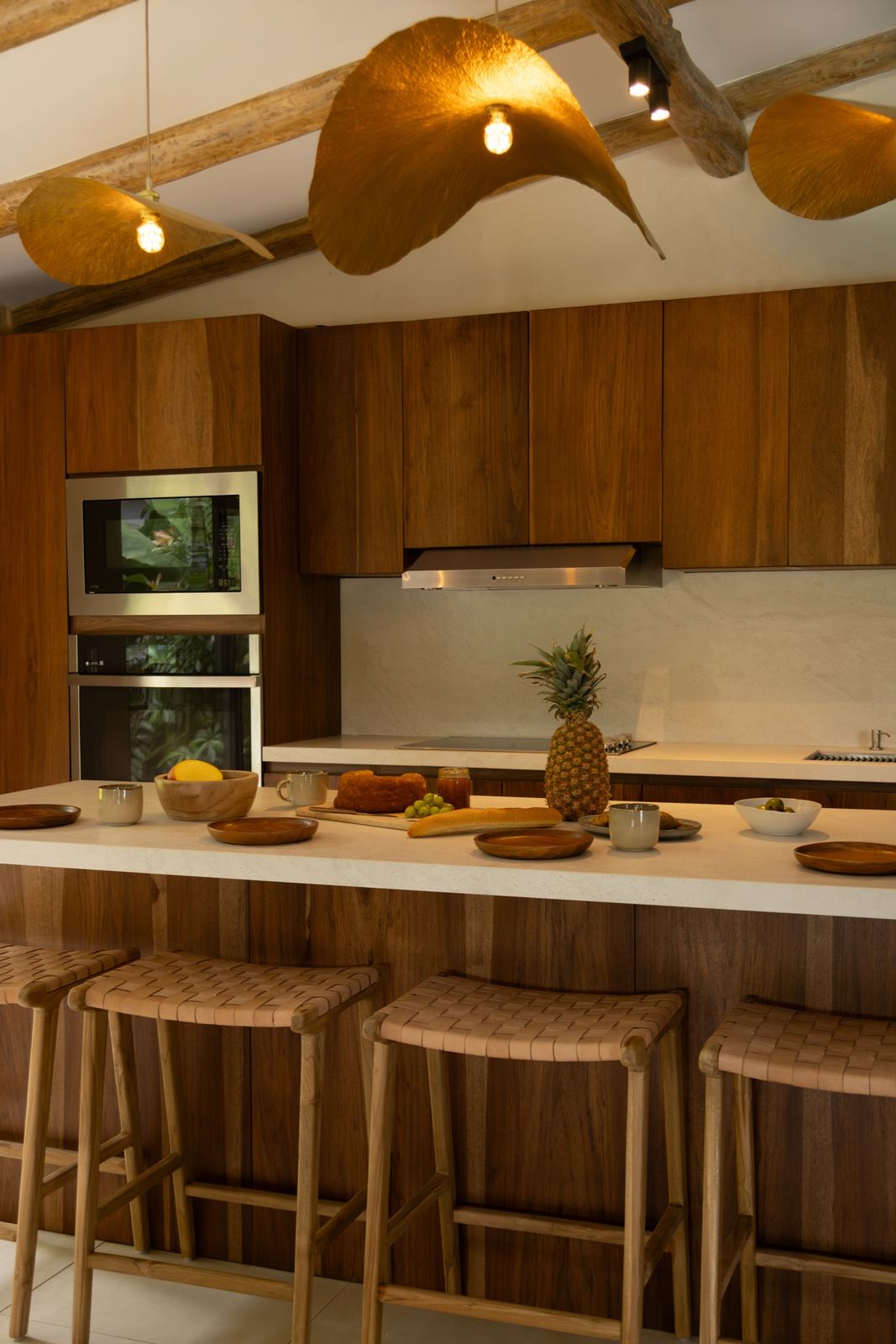 Cocina de teca de Casa Bergamota 13 con isla, bancos tejidos y lámparas doradas colgantes
