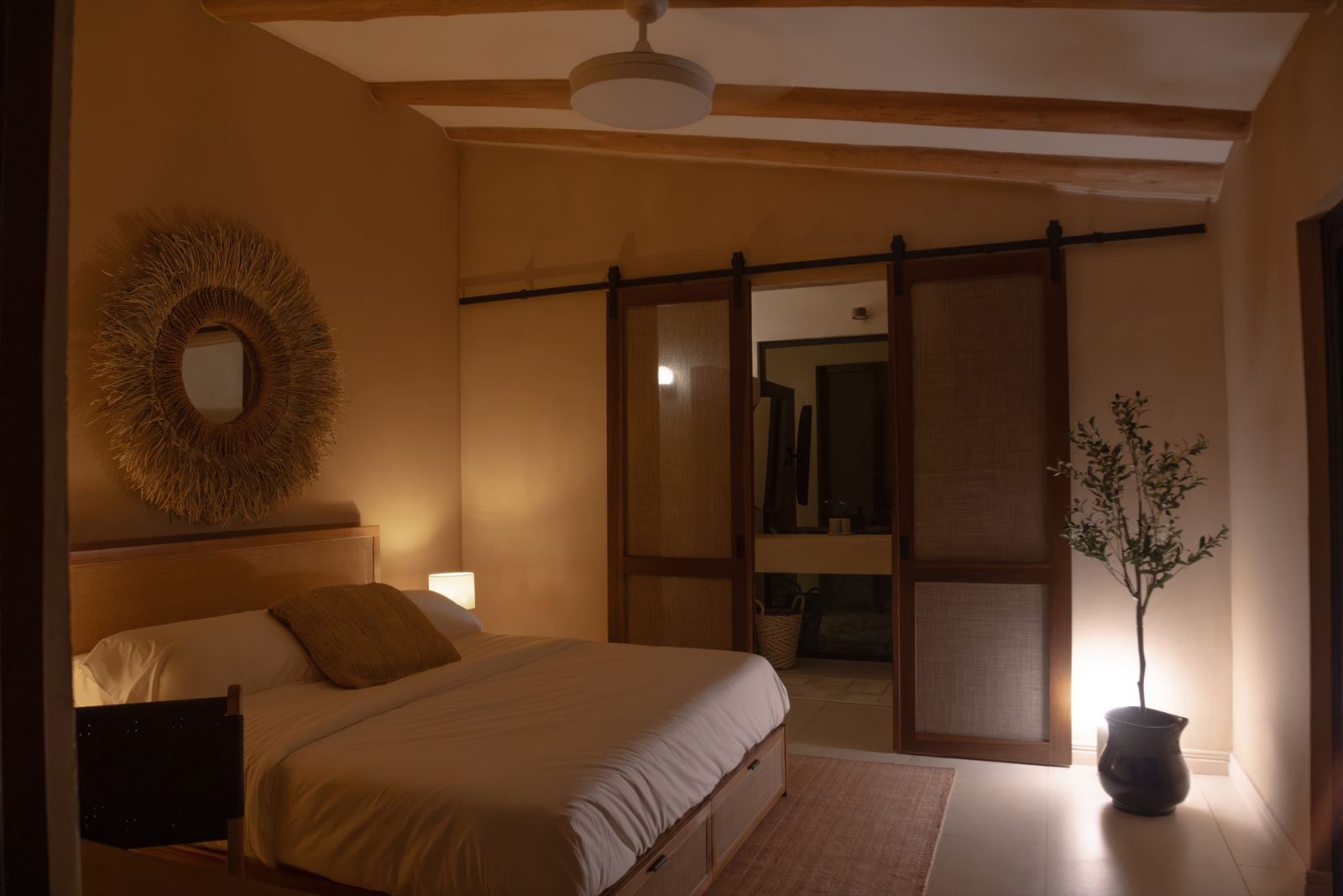 Dormitorio principal: cama, espejo de fibra tejida y puertas corredizas hacia el baño