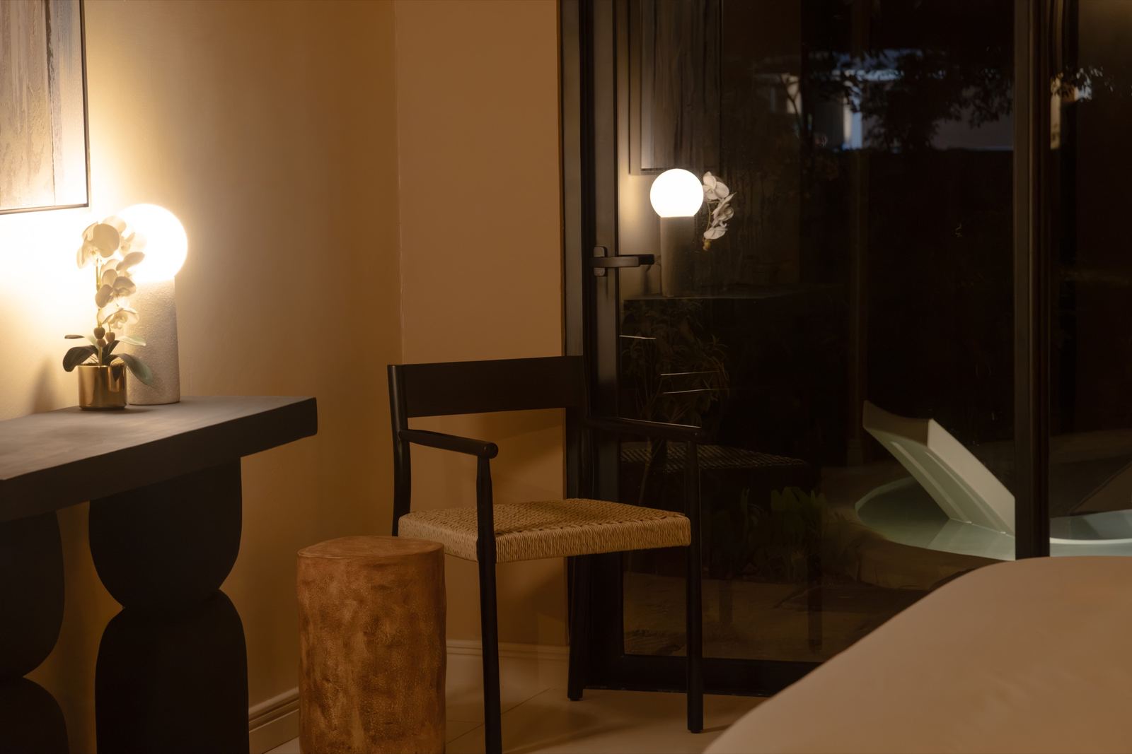 Rincón del dormitorio: consola con orquídea, silla negra y puerta de vidrio hacia la piscina