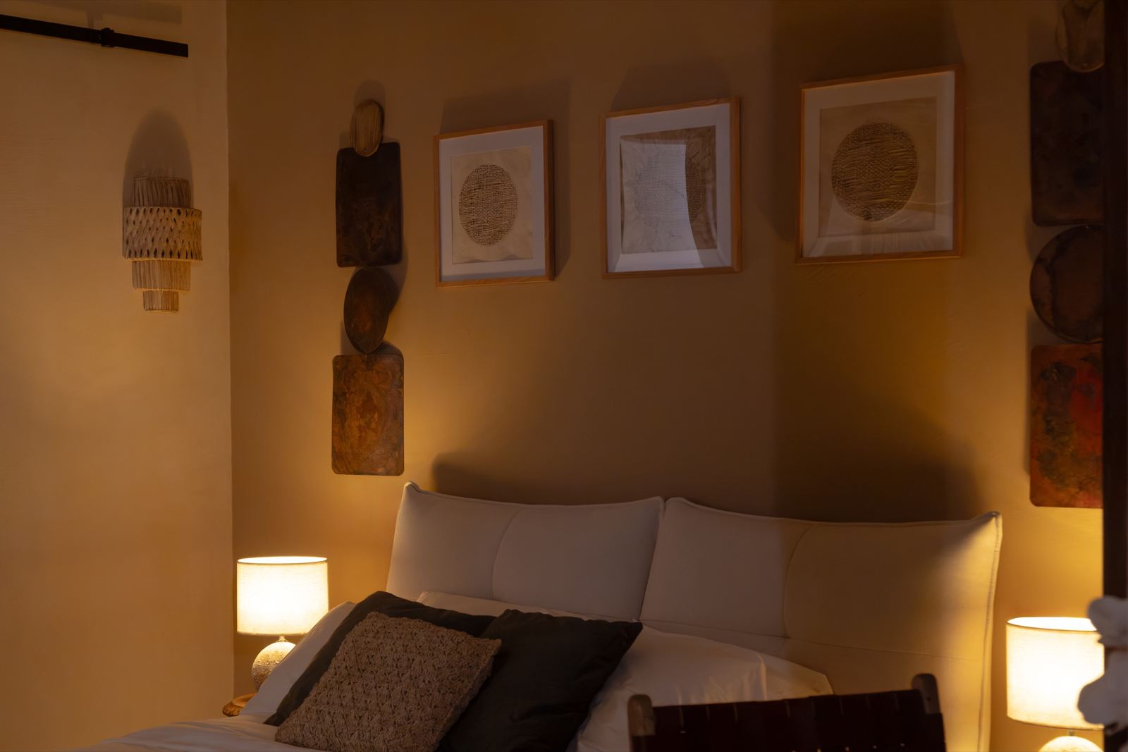 Cabecera del dormitorio con tres cuadros enmarcados, tablas de madera y lámparas de mesa