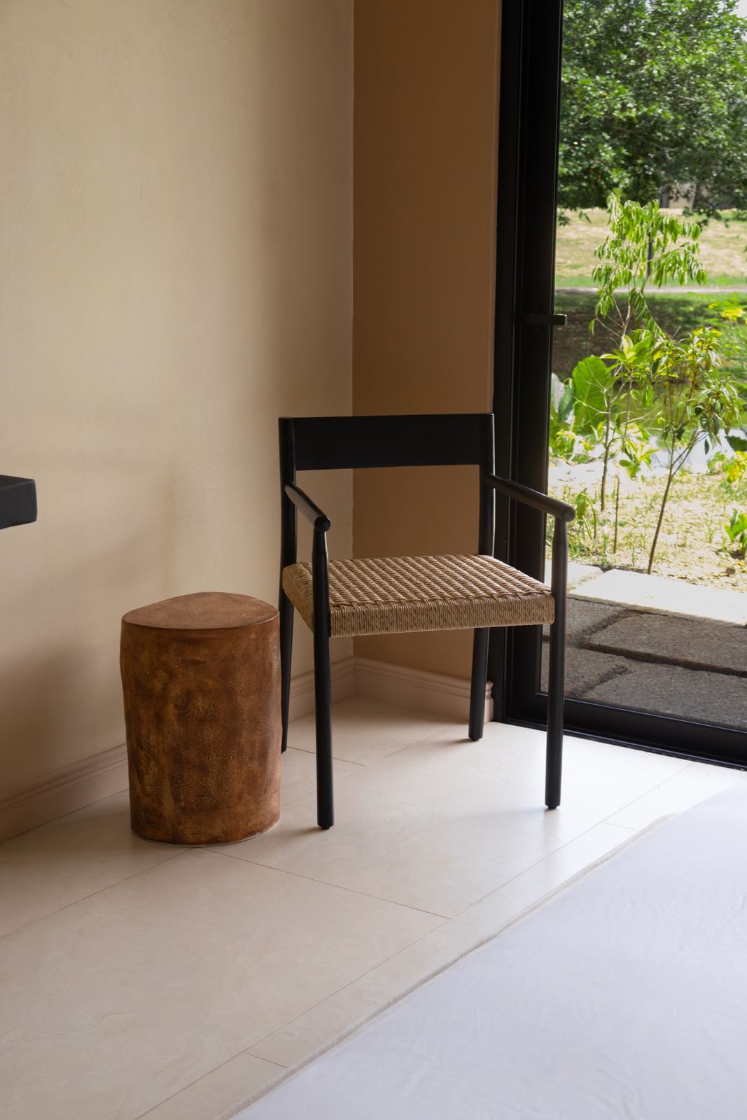 Silla negra de asiento tejido y banco de madera junto a la puerta de vidrio al jardín